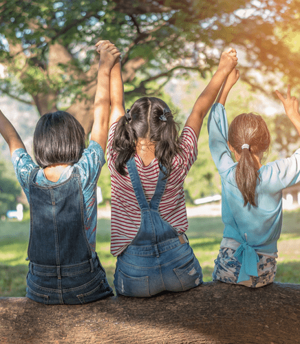 3 children with arms in the air, sitting on a tree